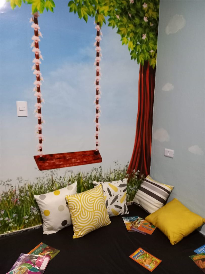 Cantinho de leitura com almofadas, mural de árvore e livros infantis